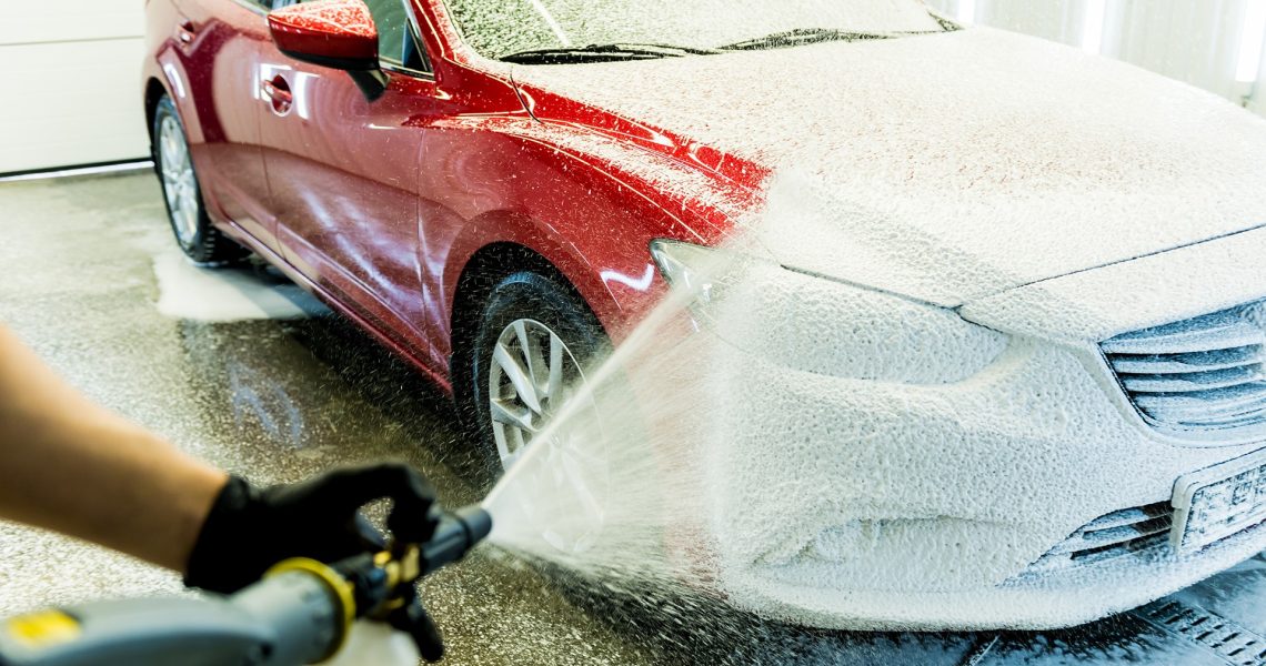 Worker washing car with active foam on a car wash