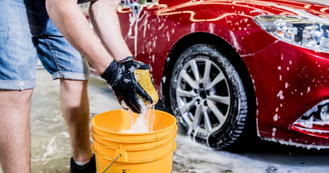 Worker washing red car with sponge on a car wash.
